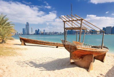 Wooden boats at beach with Abu Dhabi skyline at backdrop